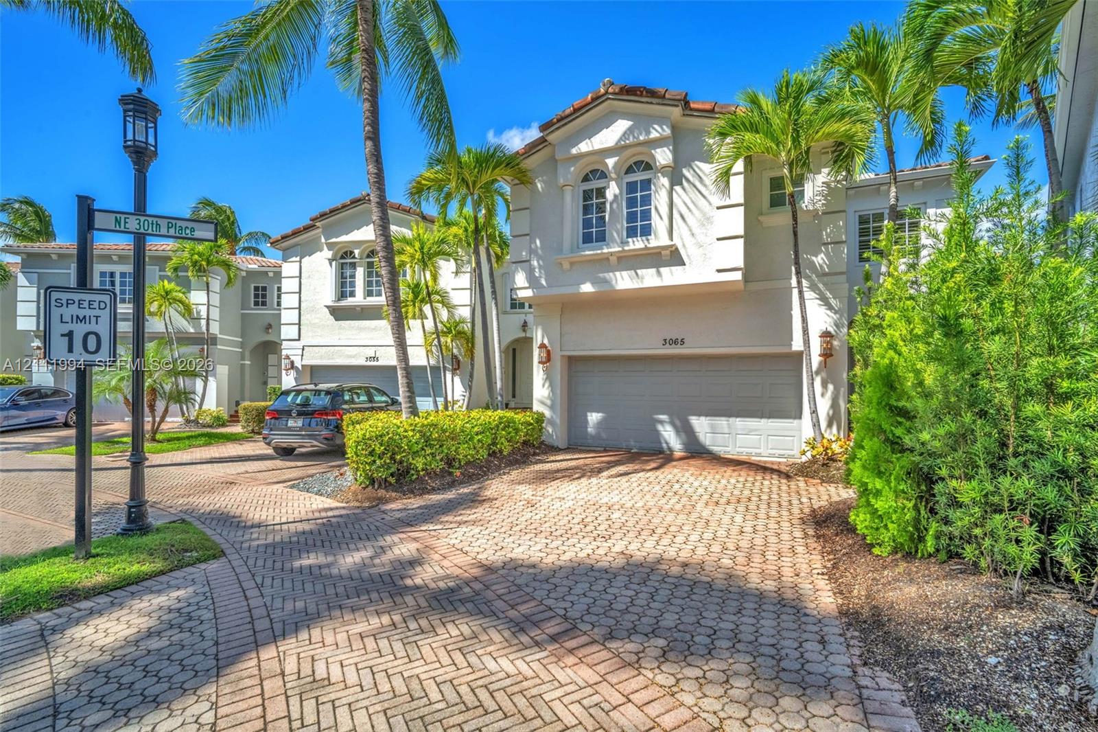 Two-story exterior featuring light-colored stucco facade, tile roof, multi-paned windows, and a paved herringbone driveway leading to an attached garage Two-story exterior featuring light-colored stucco facade, tile roof, multi-paned windows, and a paved herringbone driveway leading to an attached garage