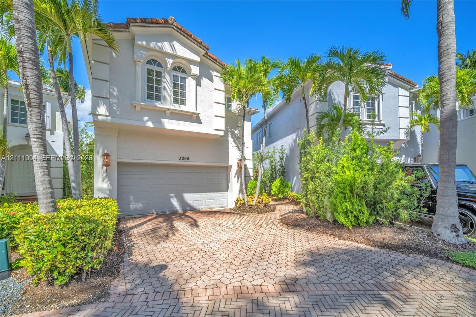 Two-story exterior featuring light-toned stucco facade, arched window detailing, an attached two-car garage, and a herringbone-patterned paved driveway