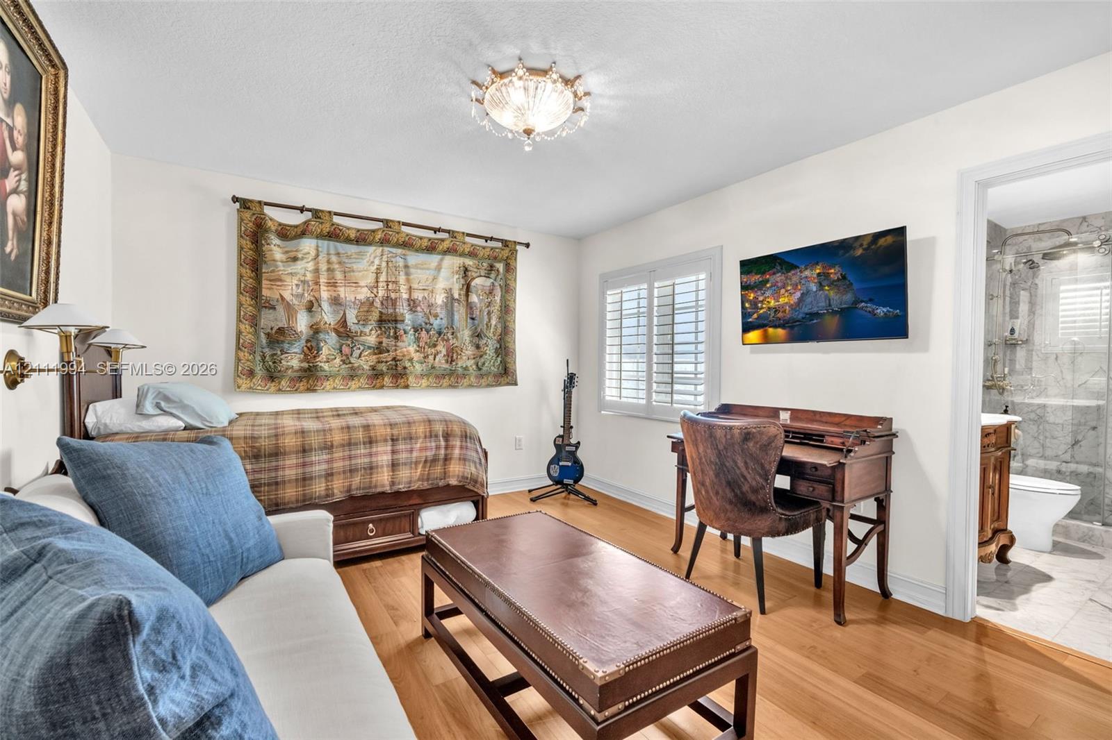 Wood-finish flooring, plantation shutters, crystal-style flush mount ceiling light, and interior wall-mounted lighting fixture