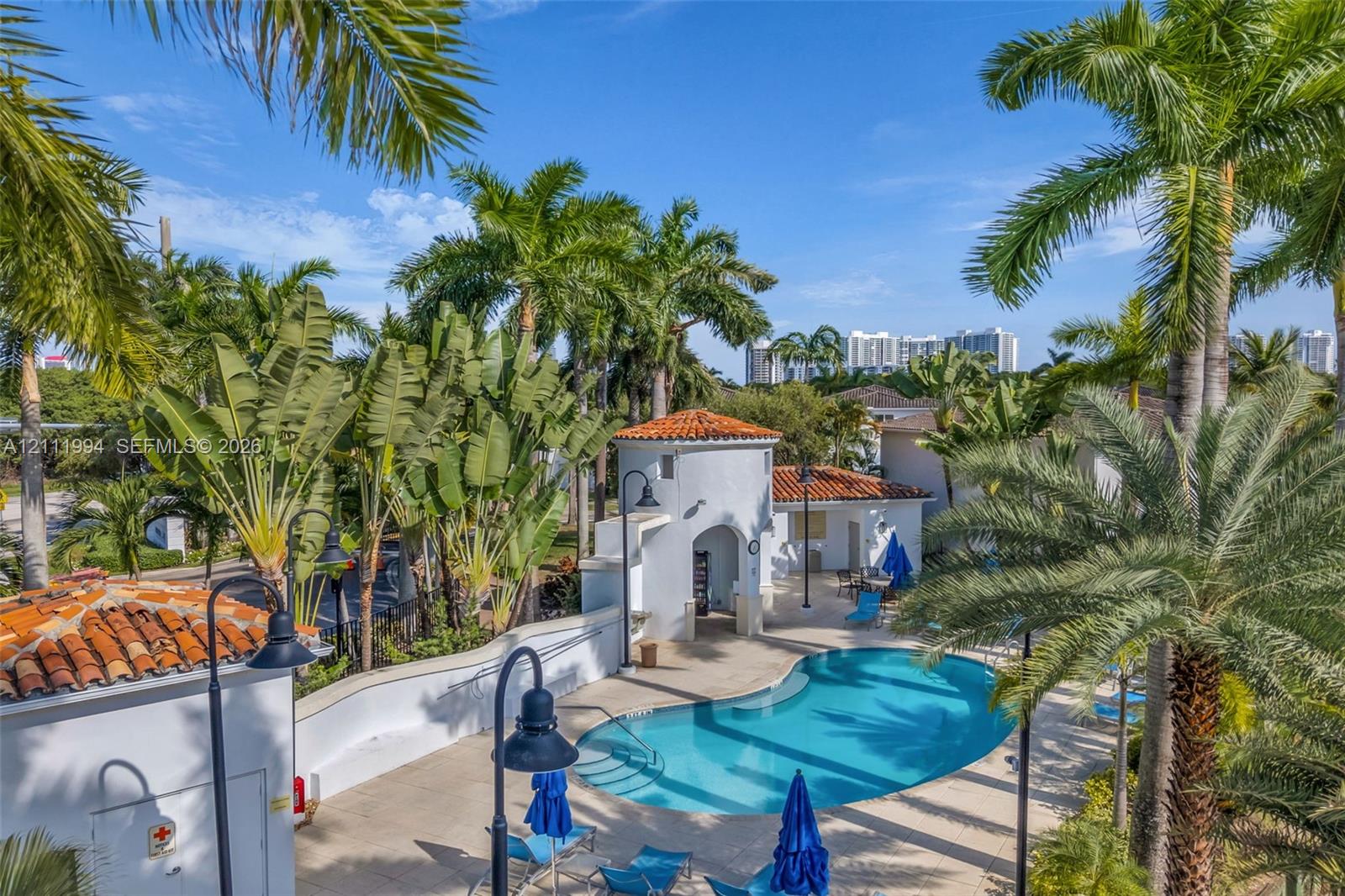 Swimming pool featuring a curved concrete deck, custom architectural tower, terracotta roof tiles, and mature landscaping