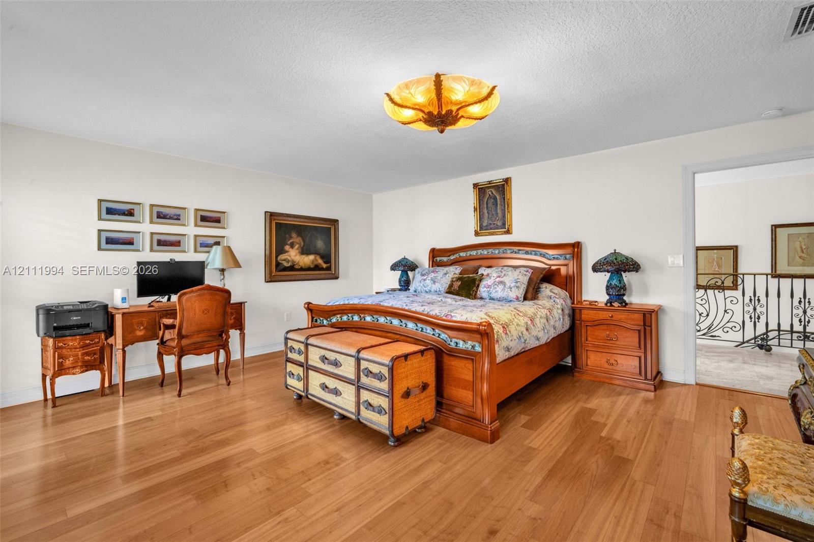 Spacious room featuring wood-finish flooring, decorative ceiling-mounted light fixture, and wrought-iron interior railing