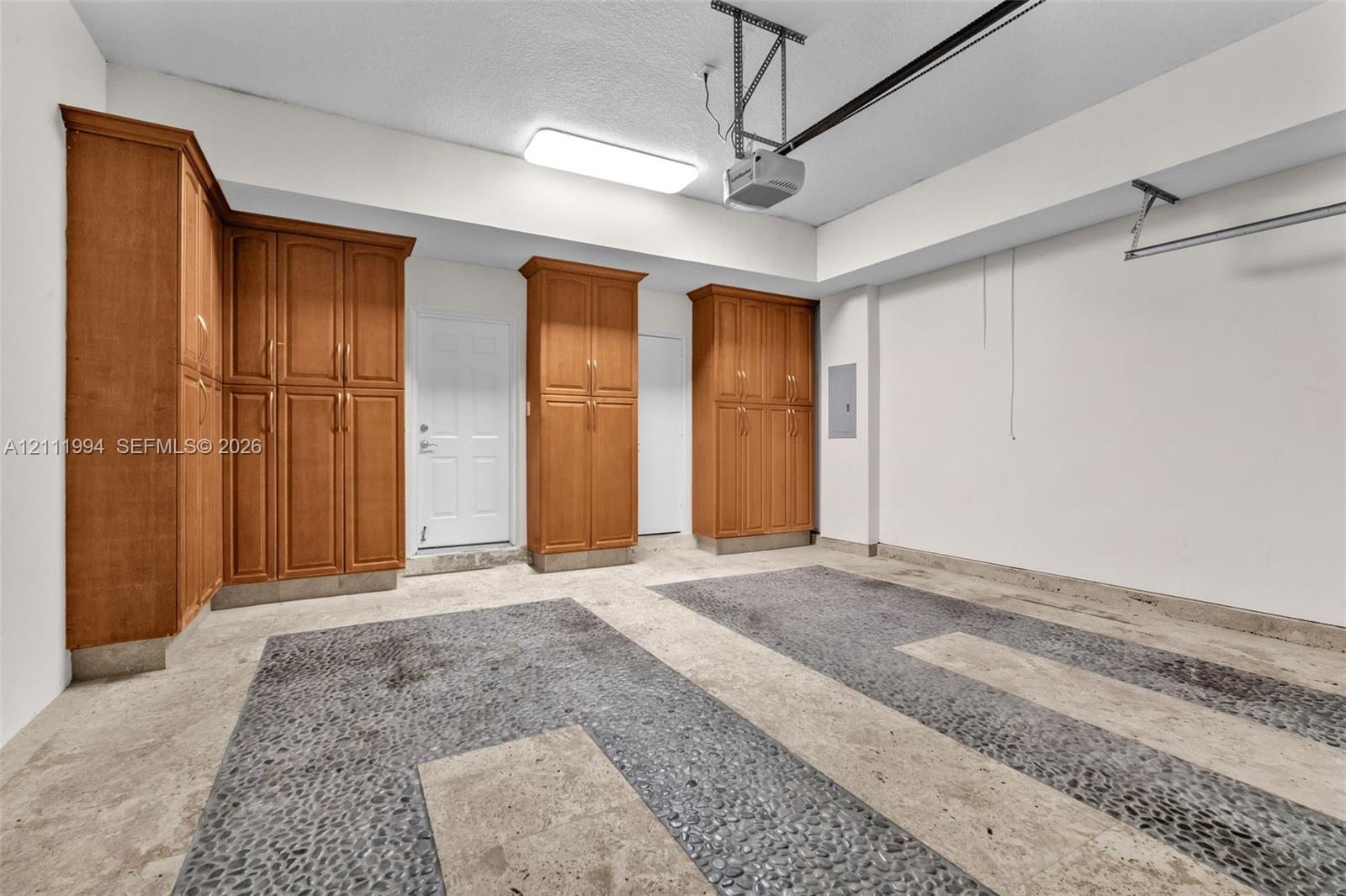 Garage featuring wood-finish cabinetry, concrete flooring with stone inlay accents, and overhead lighting