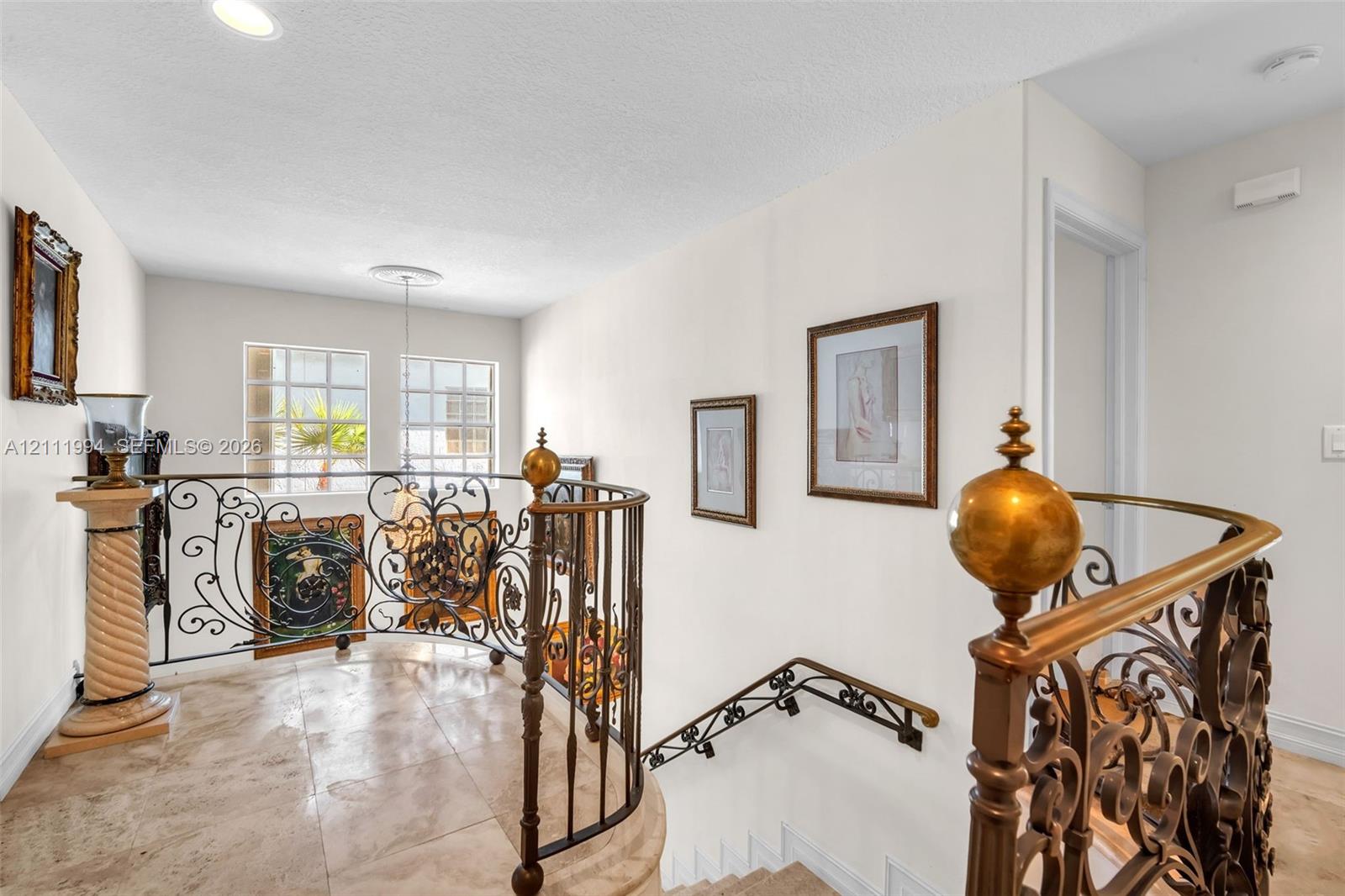 Curved staircase featuring ornate wrought iron railings with brass finials, stone flooring, and recessed ceiling lighting