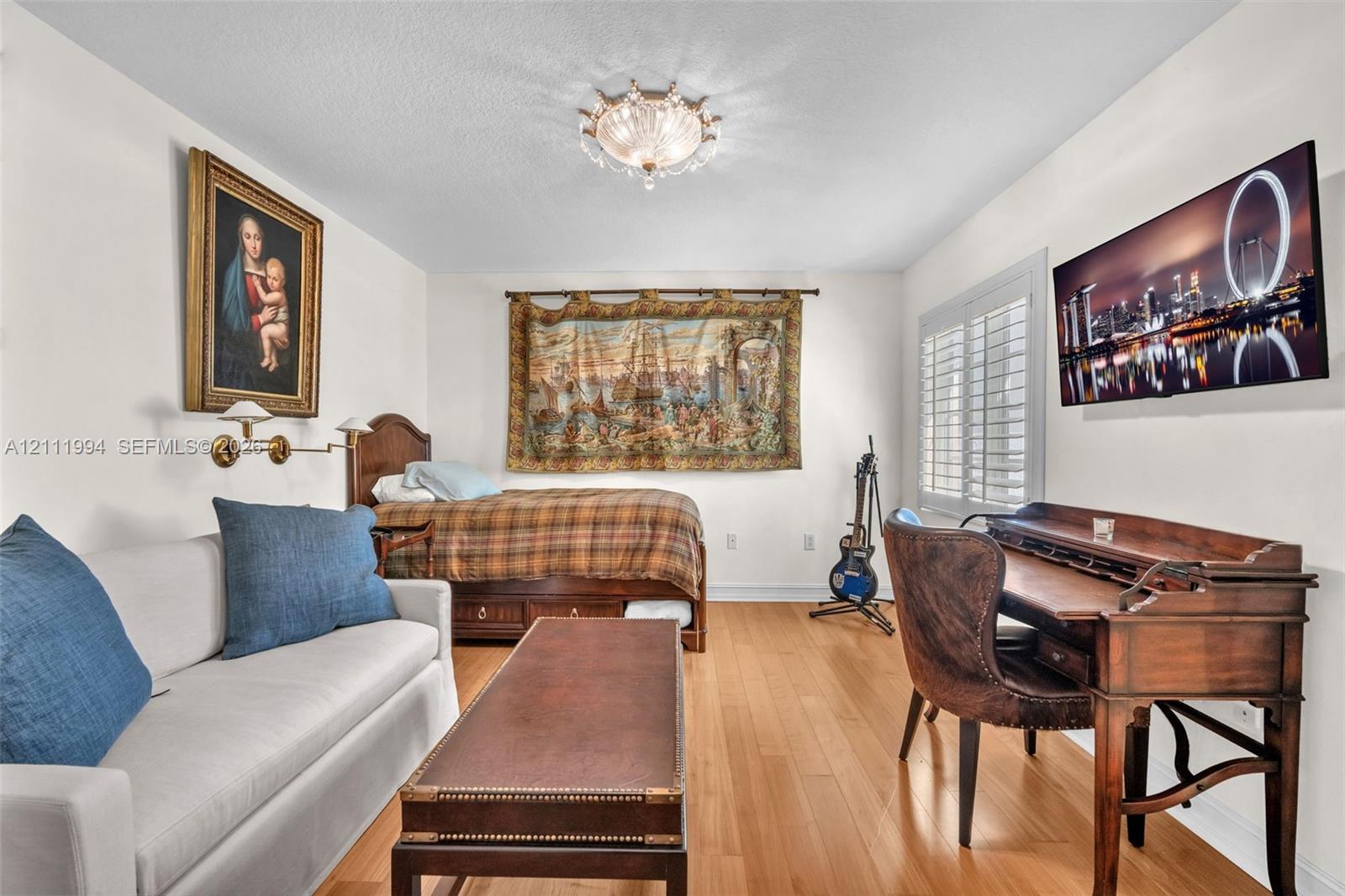 Interior space featuring wood-finish flooring, white walls, plantation shutters, and a decorative flush-mount ceiling fixture