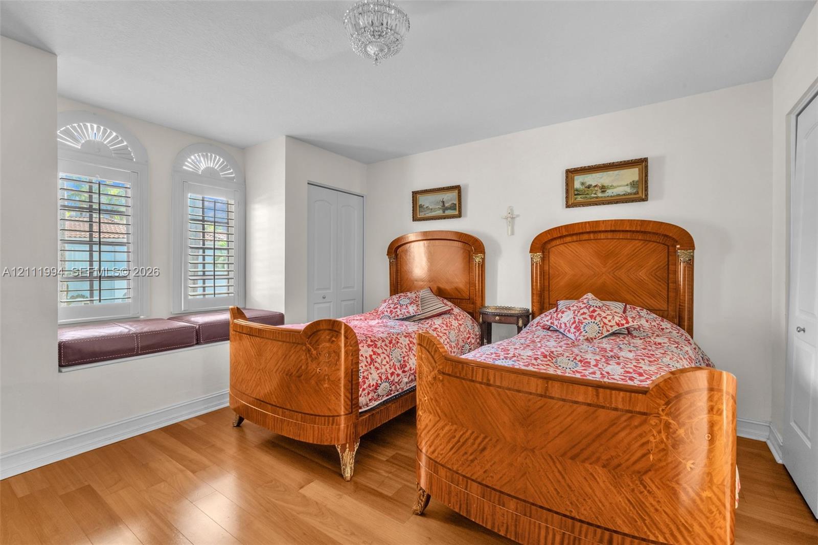 Wood-finish flooring, two arched windows with built-in window seating, and a crystal chandelier