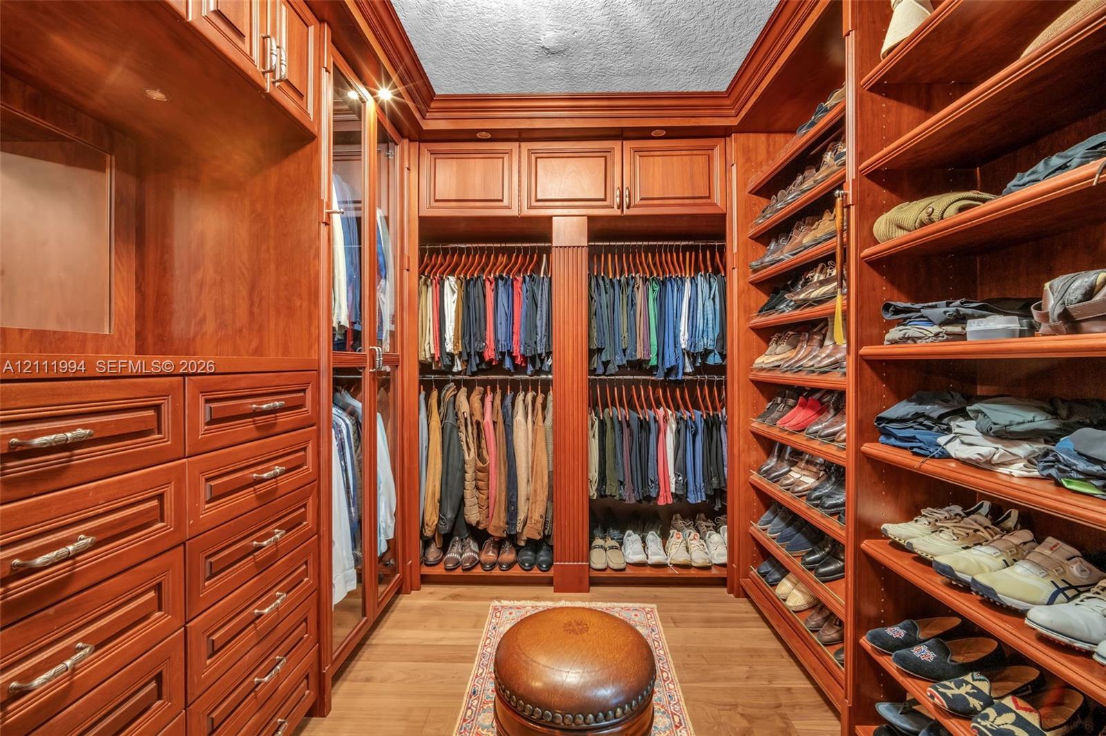 Custom walk-in closet featuring extensive cherry-toned wood cabinetry, built-in shelving, integrated hanging rods, glass-fronted wardrobe doors, and multiple tiers of drawers with metal hardware