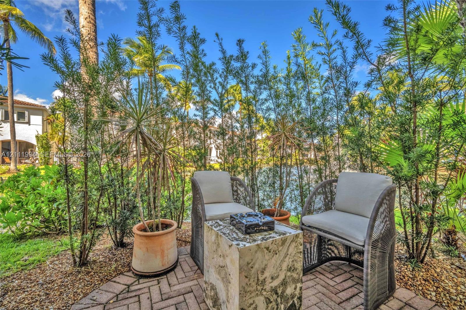 Patio area featuring brick pavers, mature landscaping, and established palm trees