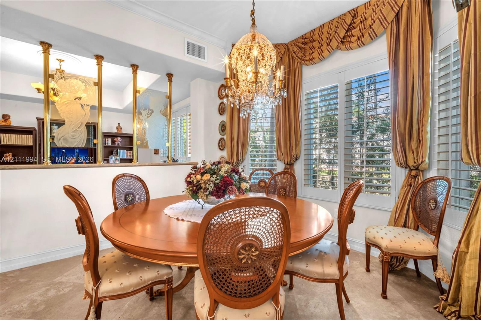 Formal dining area featuring a crystal chandelier, louvered window shutters, and a decorative partition wall with brass-finish columns and glass paneling