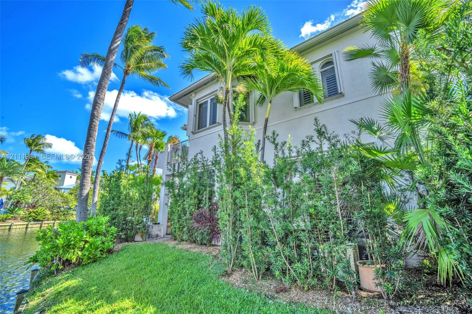 Two-story stucco exterior featuring arched windows, louvered shutters, mature palm trees, and waterfront grounds