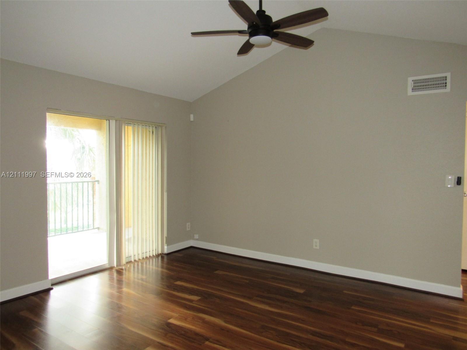 Vaulted ceilings, wood-finish flooring, ceiling fan with integrated lighting, and sliding glass door leading to a balcony
