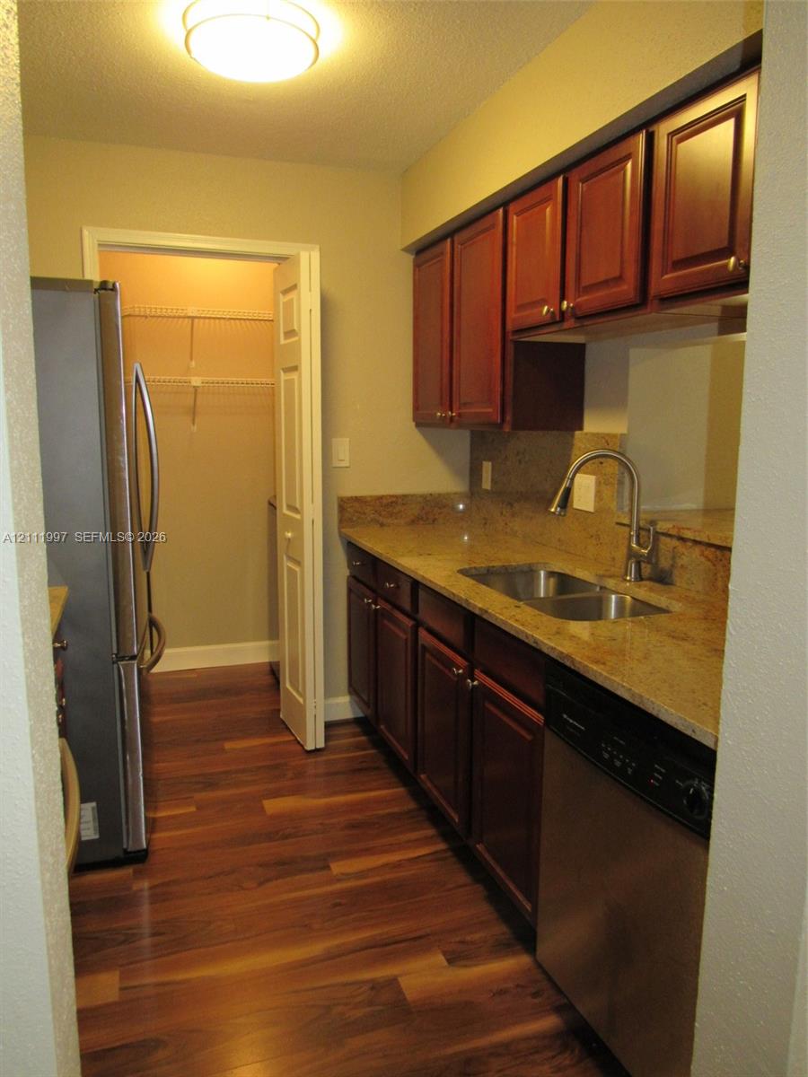 Kitchen featuring dark-toned cabinetry, natural stone countertops, stainless steel appliances, wood-finish flooring, and a walk-in pantry