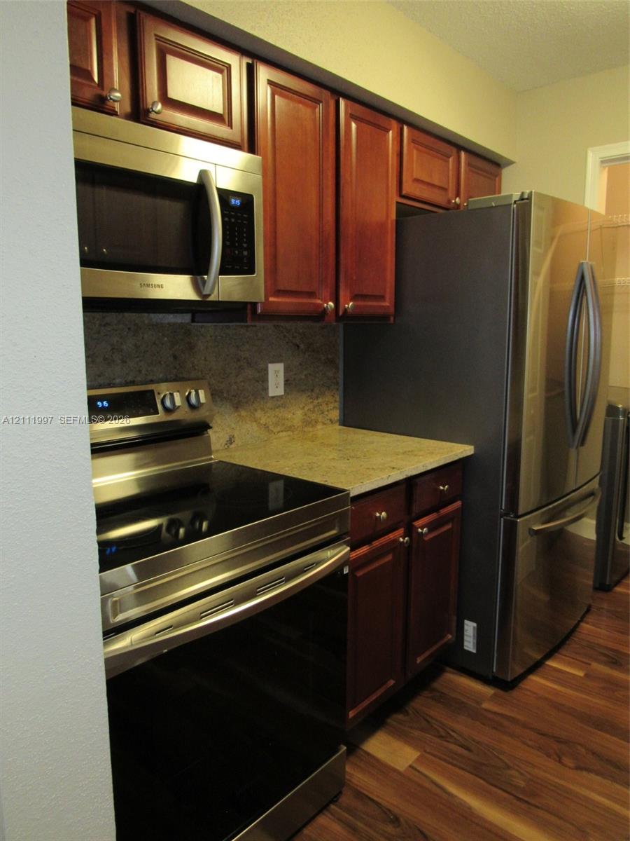 Kitchen featuring dark-toned wooden cabinetry, stone countertops, stainless steel appliances, and wood-finish flooring