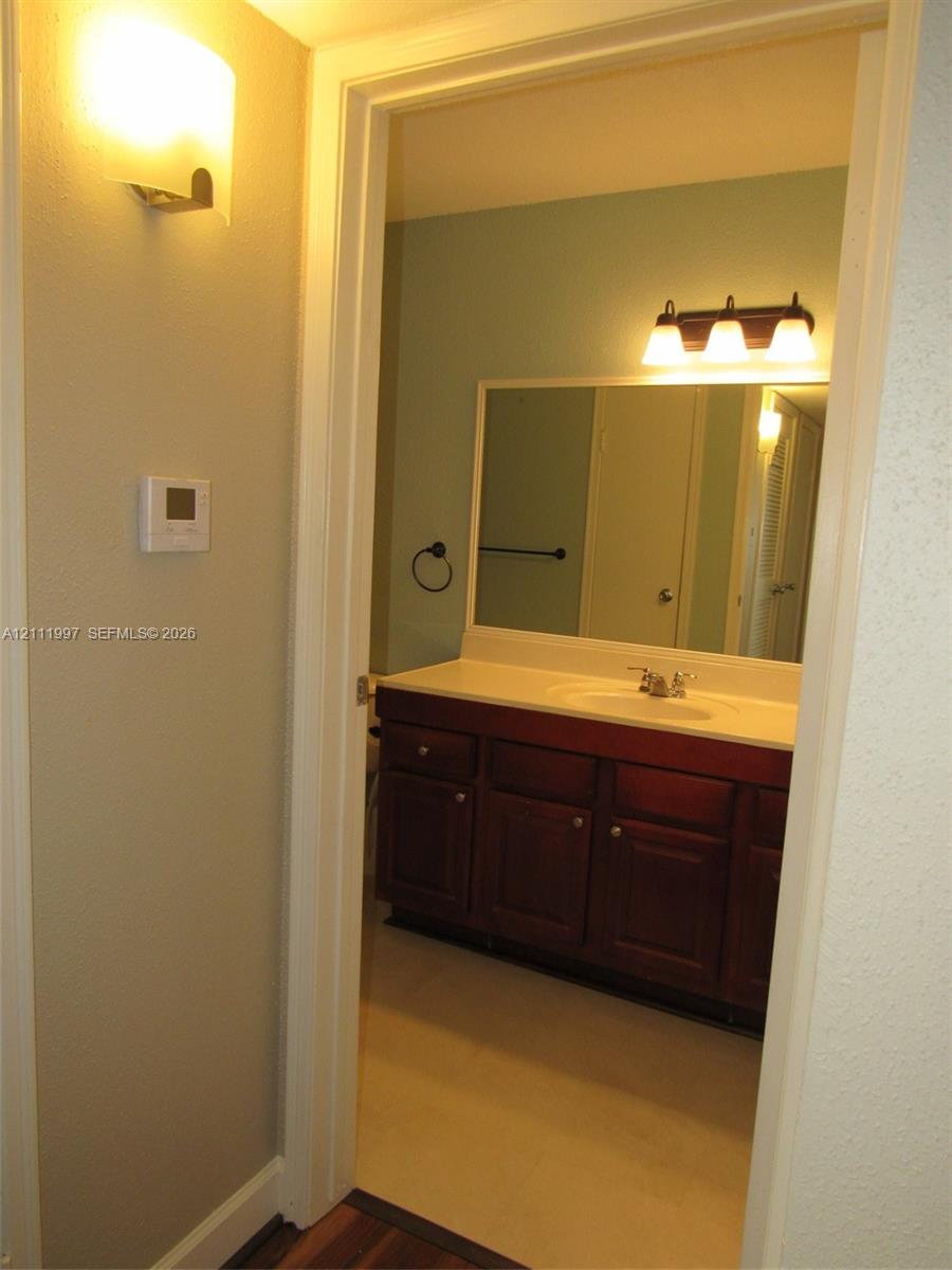 Vanity with dark wood-finish cabinetry, solid-surface countertop, integrated basin, wall-mounted three-light fixture, and large rectangular mirror