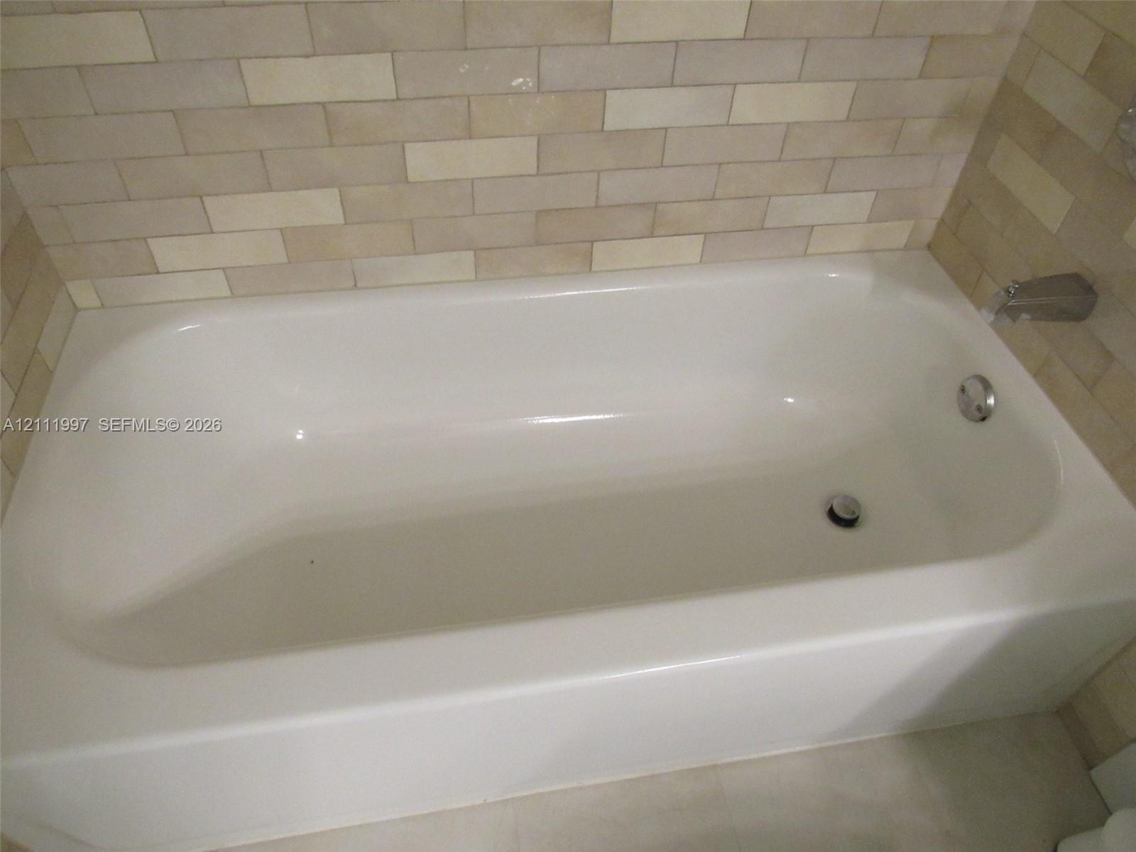 Built-in soaking tub with a smooth, white finish, chrome-plated hardware, and neutral-toned rectangular wall tile