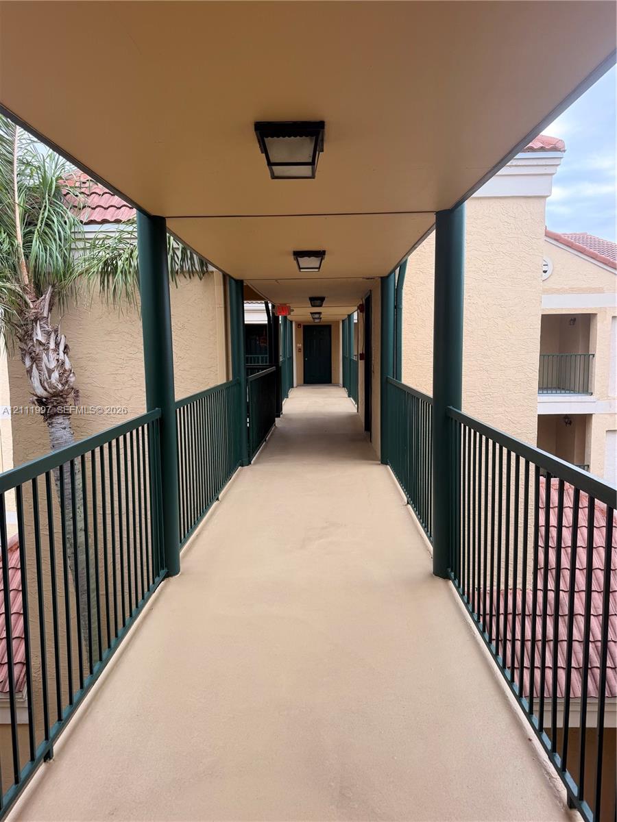 Covered exterior walkway featuring dark metal railings, neutral-tone stucco finishes, and flush-mount overhead lighting