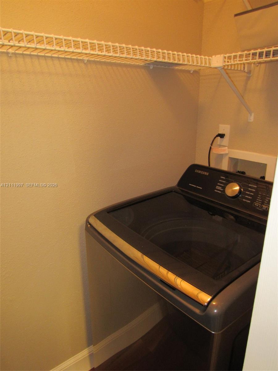 Laundry alcove featuring a top-load washer, wall-mounted electrical outlet, plumbing connection box, and overhead wire shelving