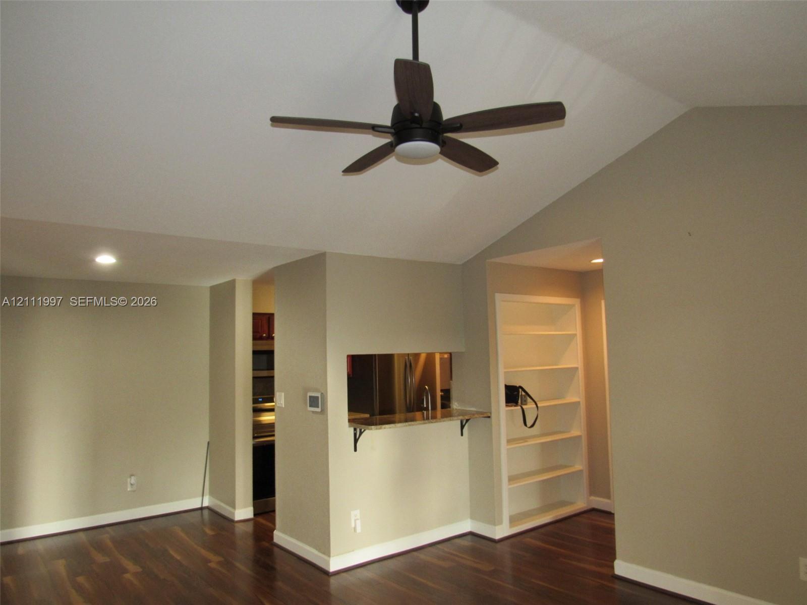 Vaulted ceilings, wood-finish flooring, built-in shelving, and a pass-through opening with stone-surface counter