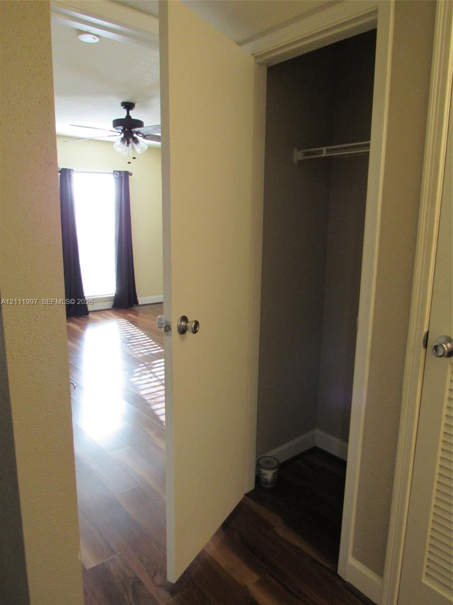 Interior space featuring wood-finish flooring, a built-in closet with overhead shelving, and a ceiling fan with integrated lighting