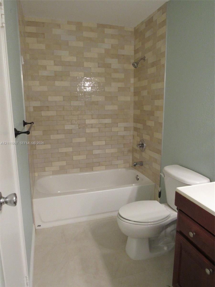 Bathroom featuring a tub-shower combination with multi-toned rectangular tile surround, a built-in dark wood vanity, and a high-profile toilet