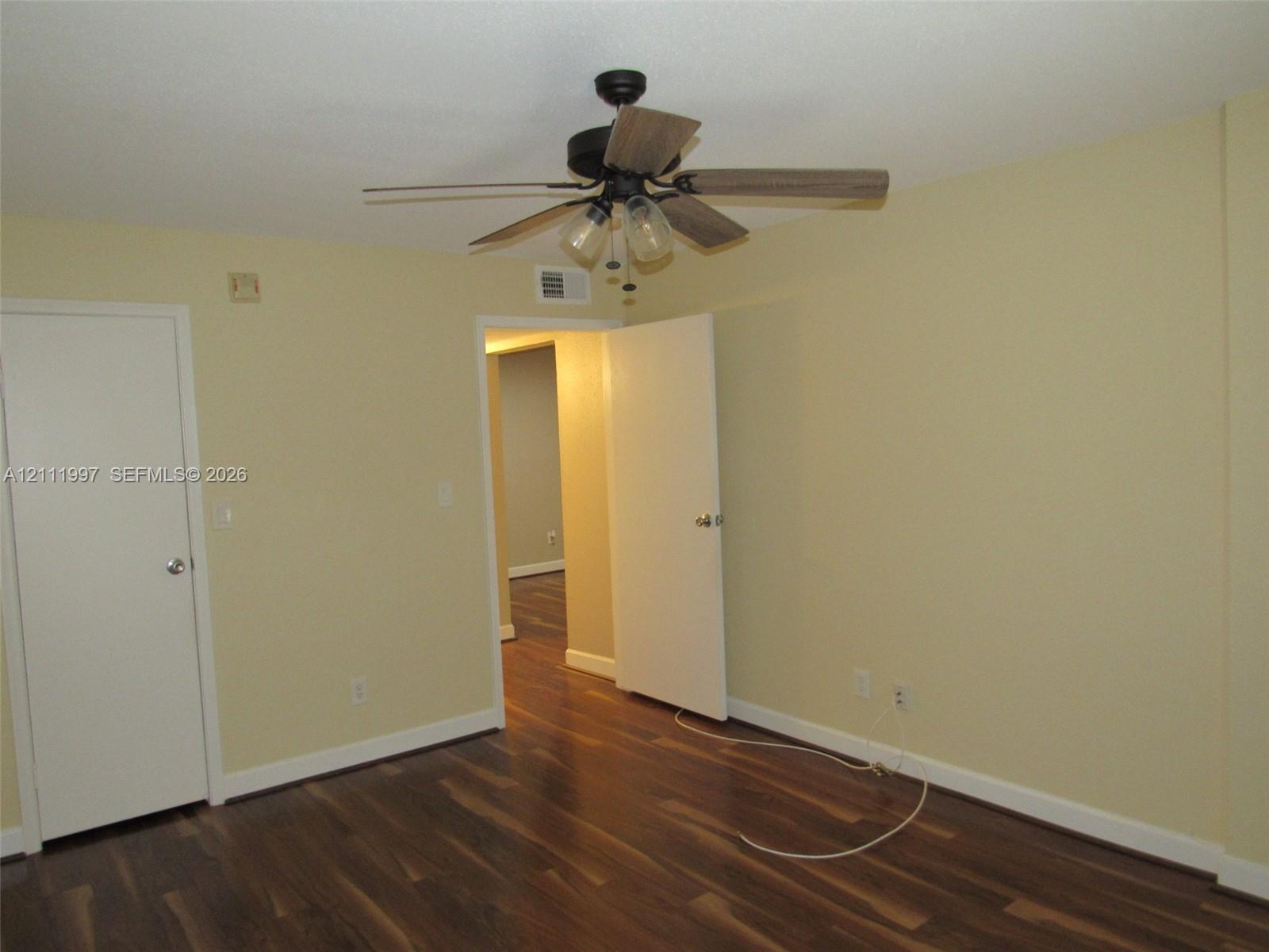 Room featuring wood-finish flooring, a ceiling fan with multi-light fixture, and two interior doors