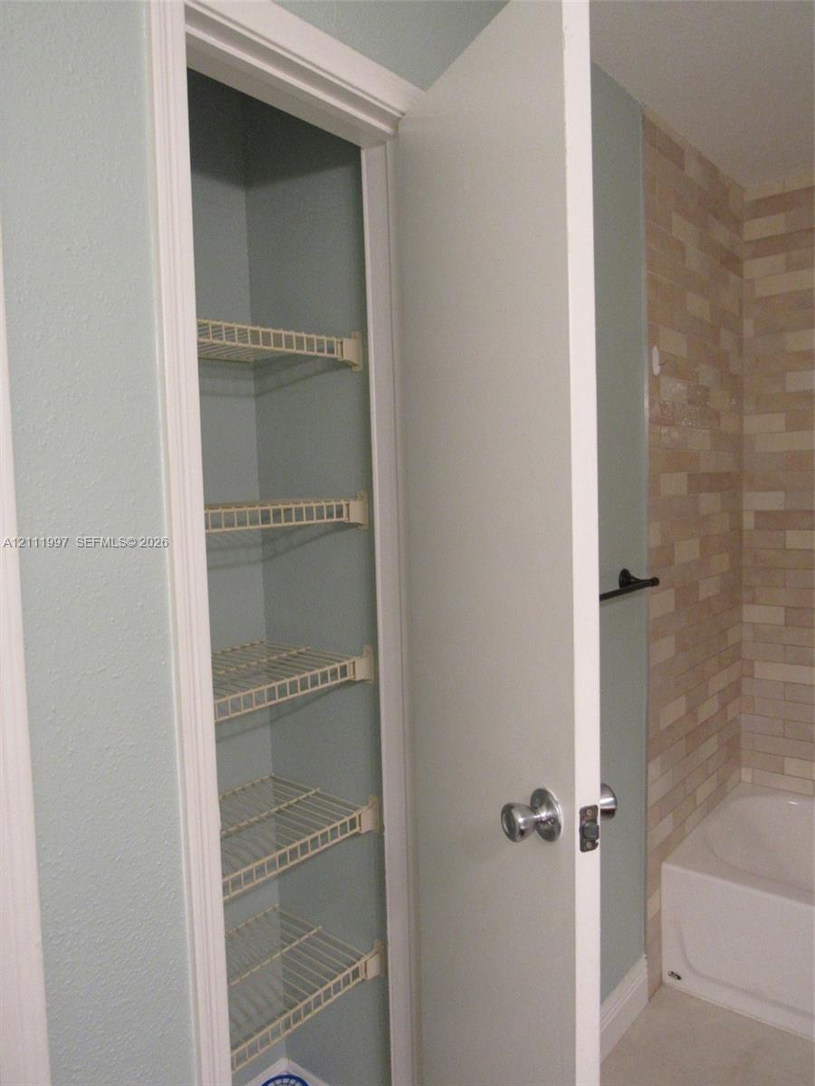 Built-in storage closet featuring five wire shelving tiers, complemented by a matte black towel bar and textured stone-finish wall tile surrounding the bathtub