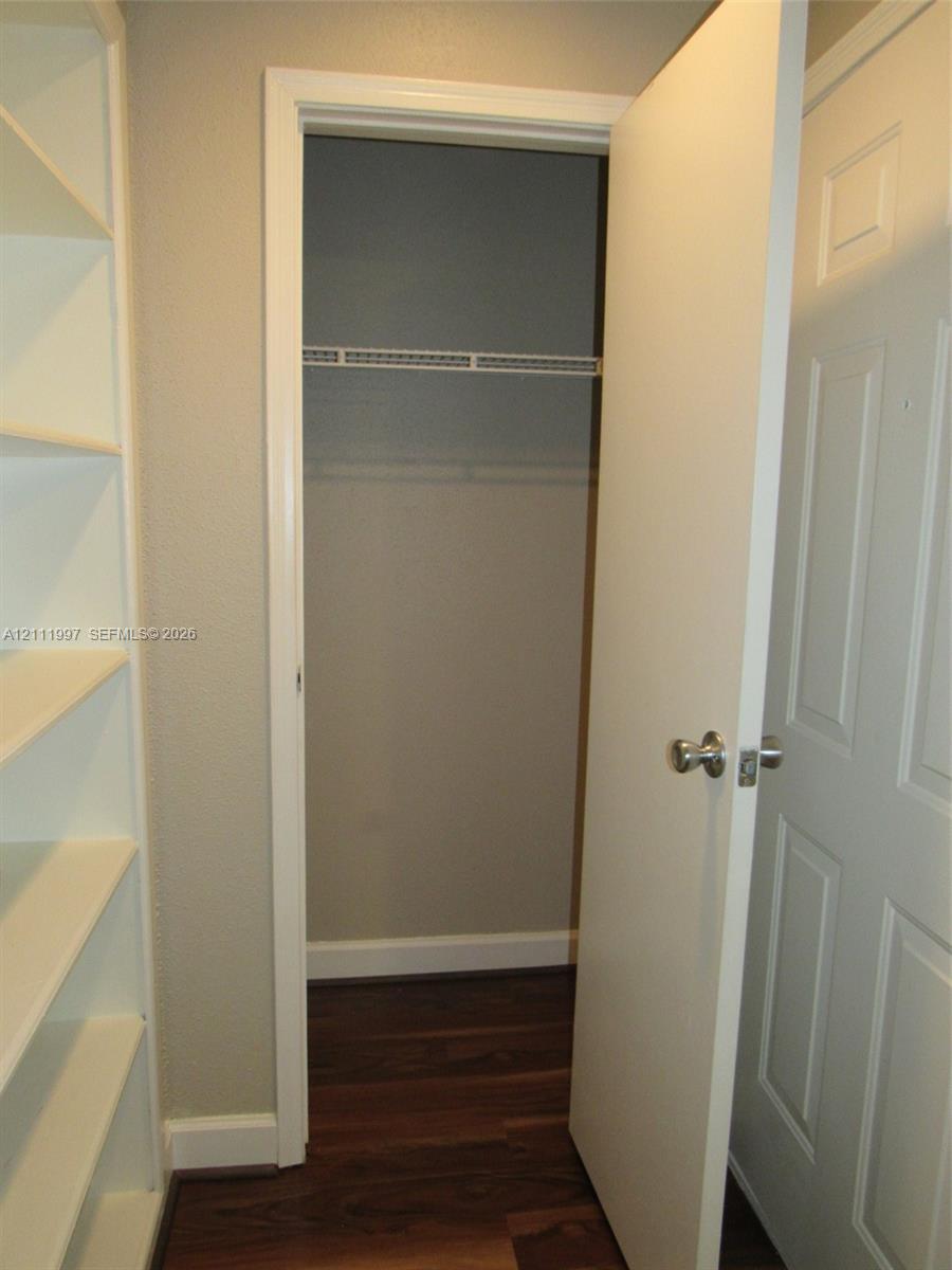 Built-in white shelving unit, wood-finish flooring, and closet featuring a wire hanging rack