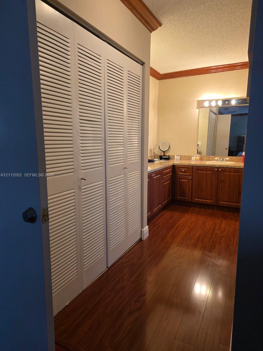 Wood-finish flooring, white louvered bifold closet doors, dark wood-finish cabinetry, stone-finish countertop, and wall-mounted vanity lighting
