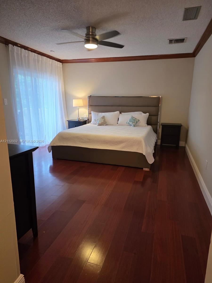 Wood-finish flooring, ceiling fan with integrated lighting, crown molding, and sliding glass doors