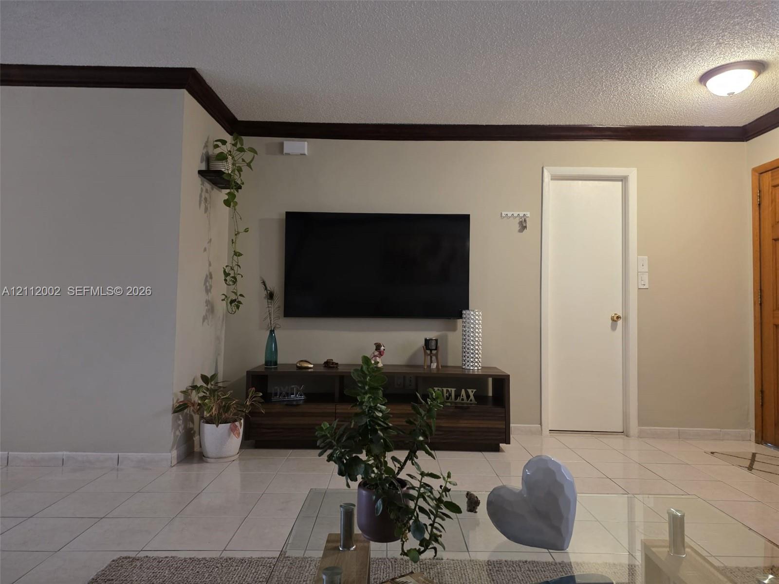 Neutral-toned interior space featuring contrasting dark wood crown molding, light-colored tile flooring, and a solid-core interior door