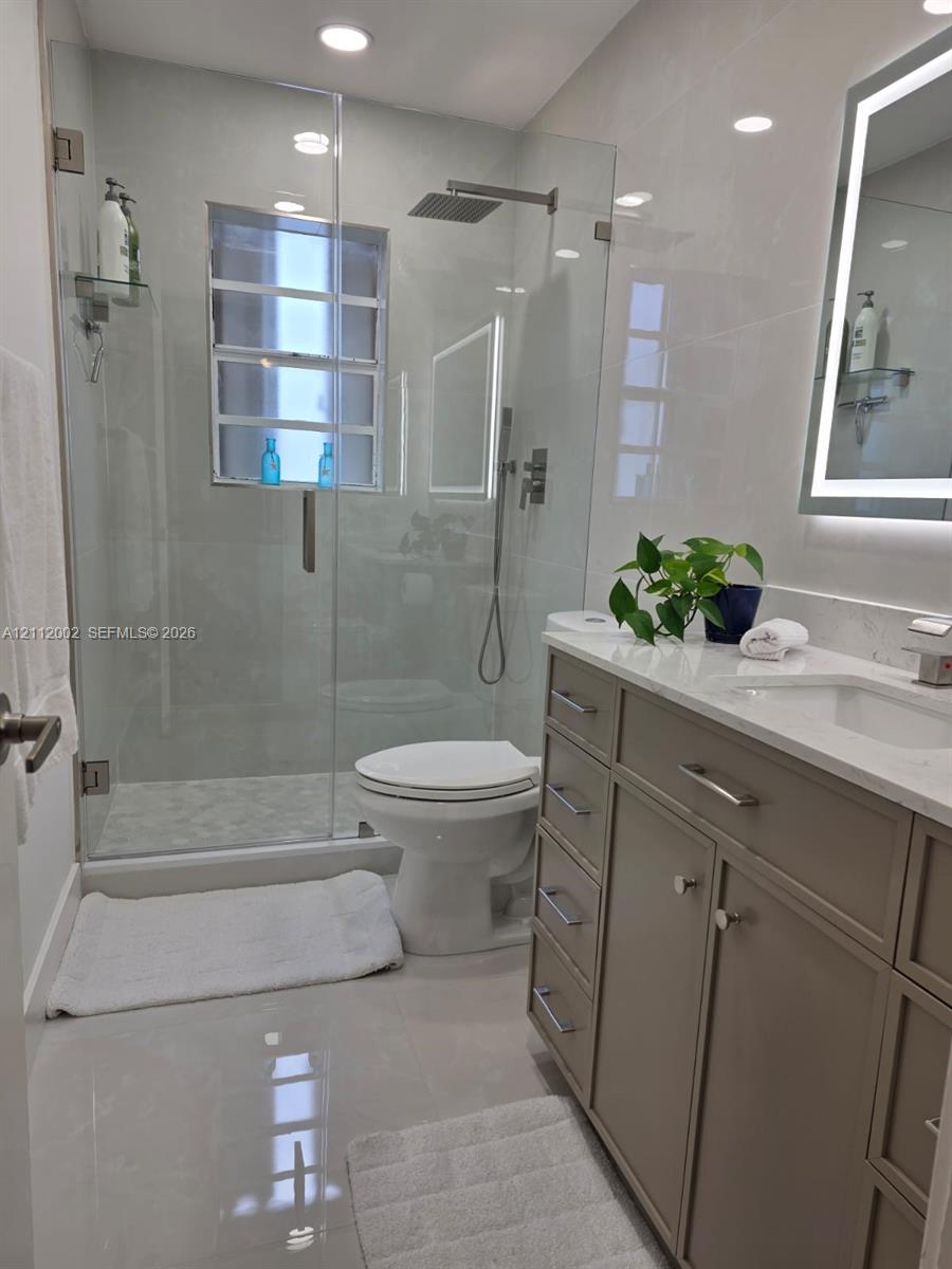Walk-in shower with frameless glass enclosure, rainfall showerhead, and integrated stone-style tile surround