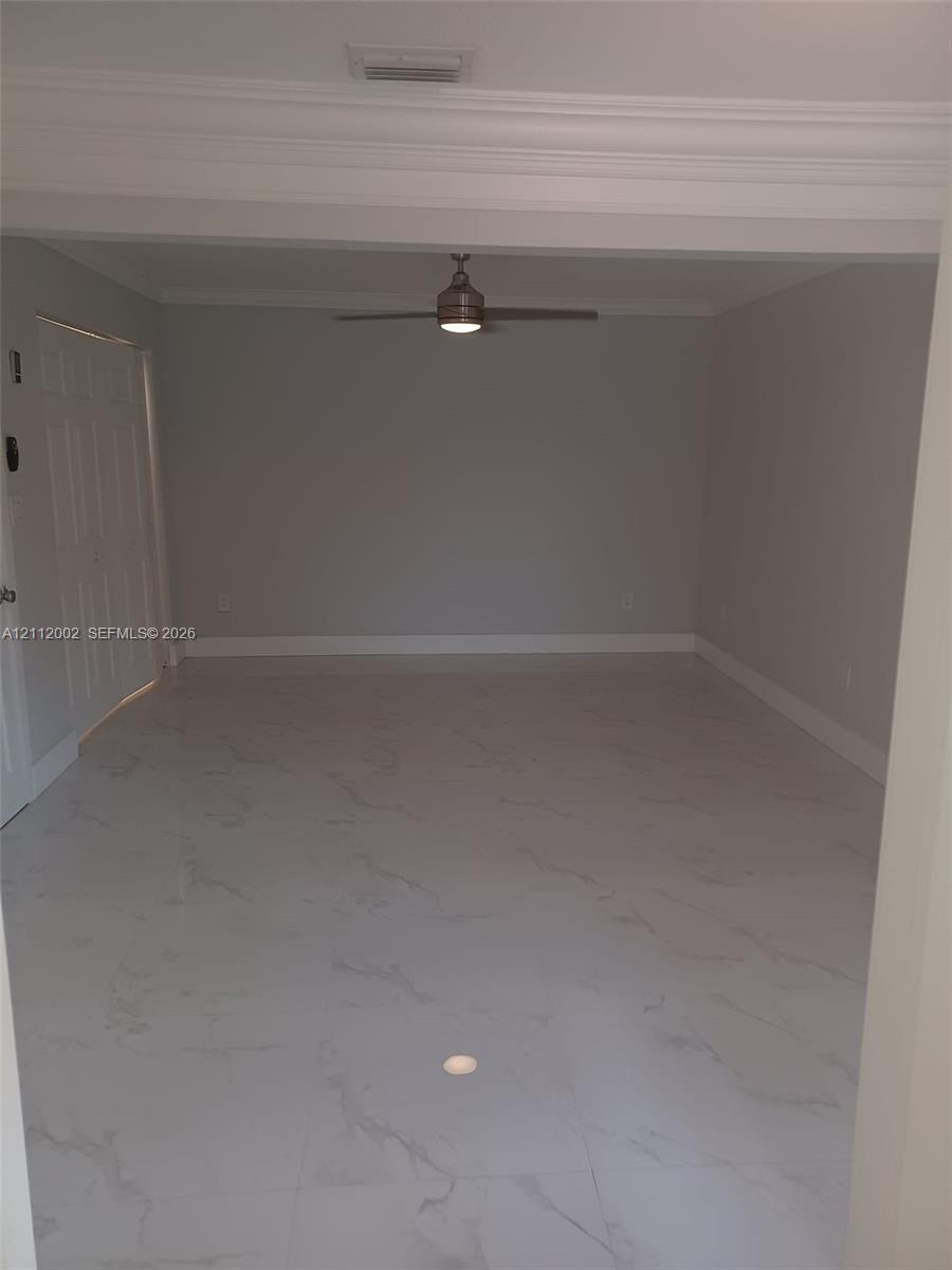 Neutral-toned interior space featuring large-format stone-patterned floor tile, crown molding, and a central ceiling fan