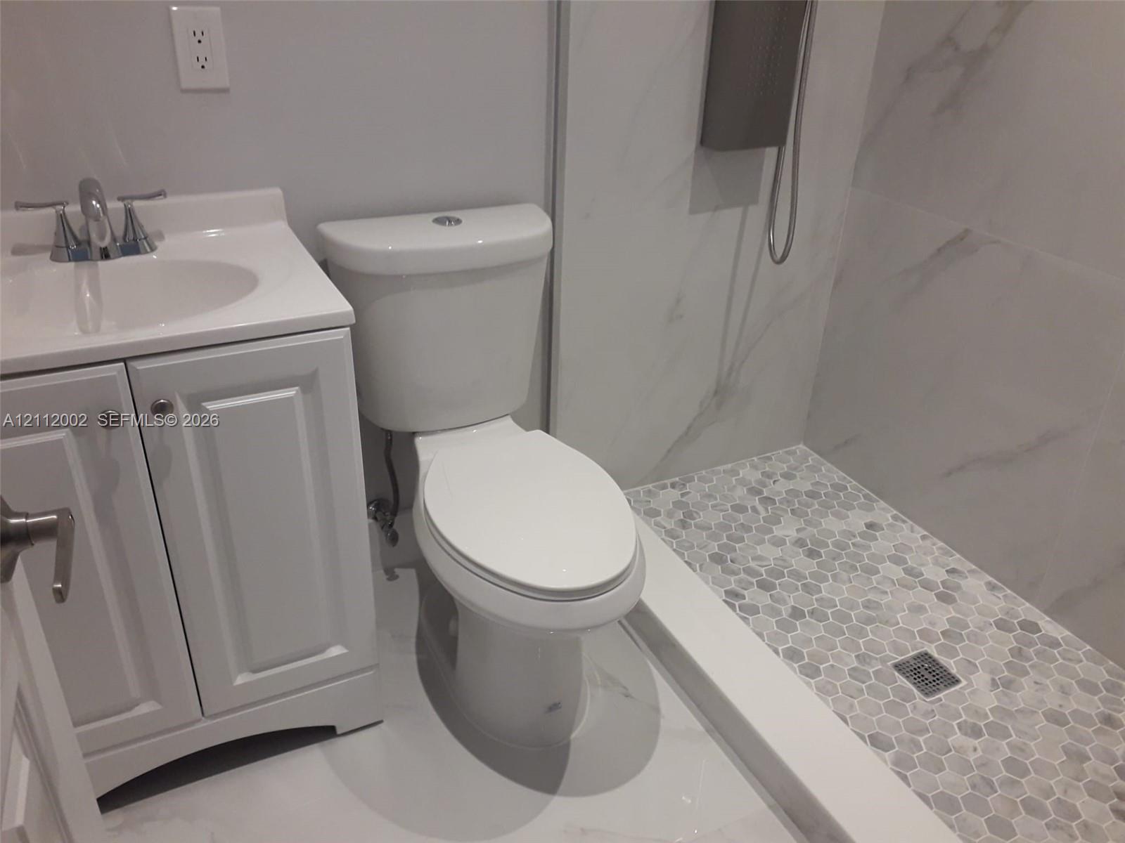 Bathroom featuring a white vanity cabinet with a integrated sink, two-piece toilet, and a walk-in shower with large-format wall tile and a hexagonal tile floor