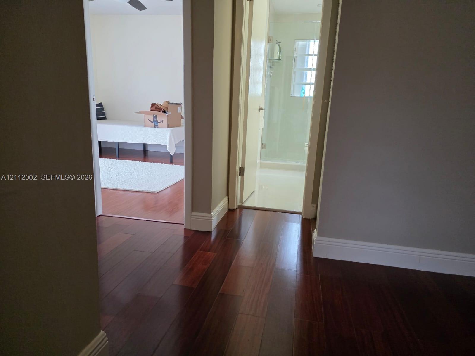 Rich-toned wood-finish flooring, glass-enclosed shower, and neutral wall tones