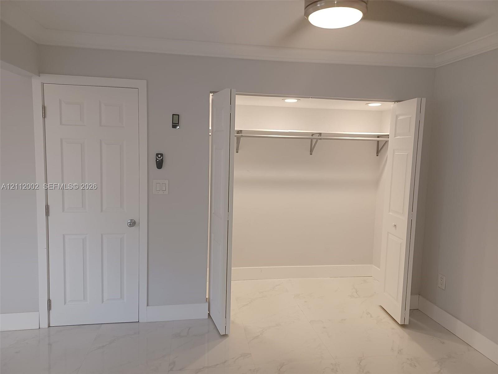 Walk-in closet featuring built-in shelving and recessed lighting, paired with polished stone-finish flooring and a white paneled door
