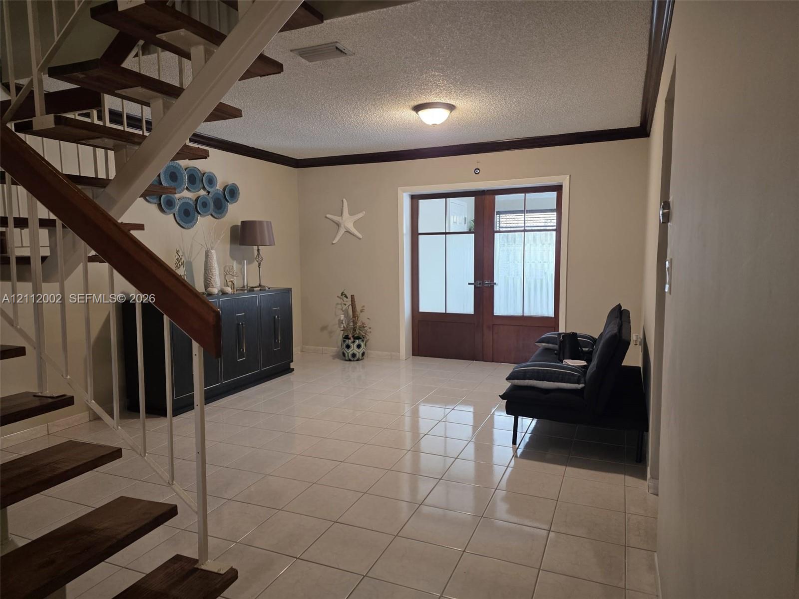 Open foyer featuring wood-tread staircase, white metal railings, ceramic tile flooring, and double-entry doors with glass paneling Open foyer featuring wood-tread staircase, white metal railings, ceramic tile flooring, and double-entry doors with glass paneling