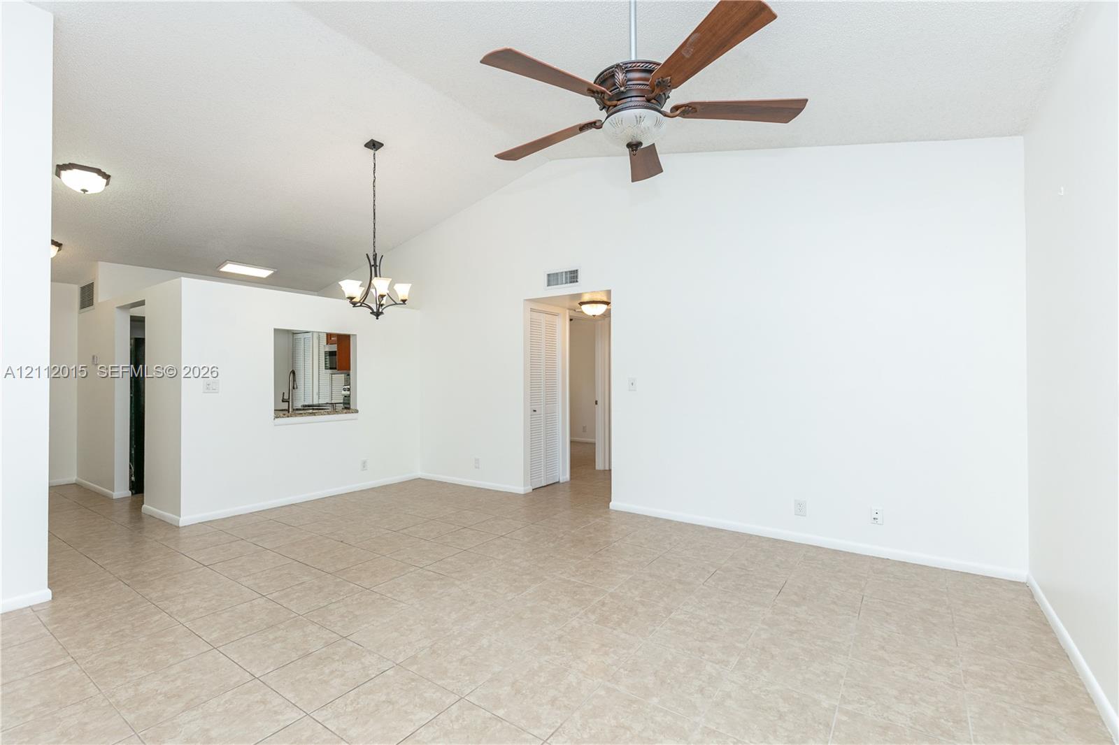 Vaulted ceilings featuring a central ceiling fan, neutral tile flooring, a decorative chandelier, and a kitchen pass-through window