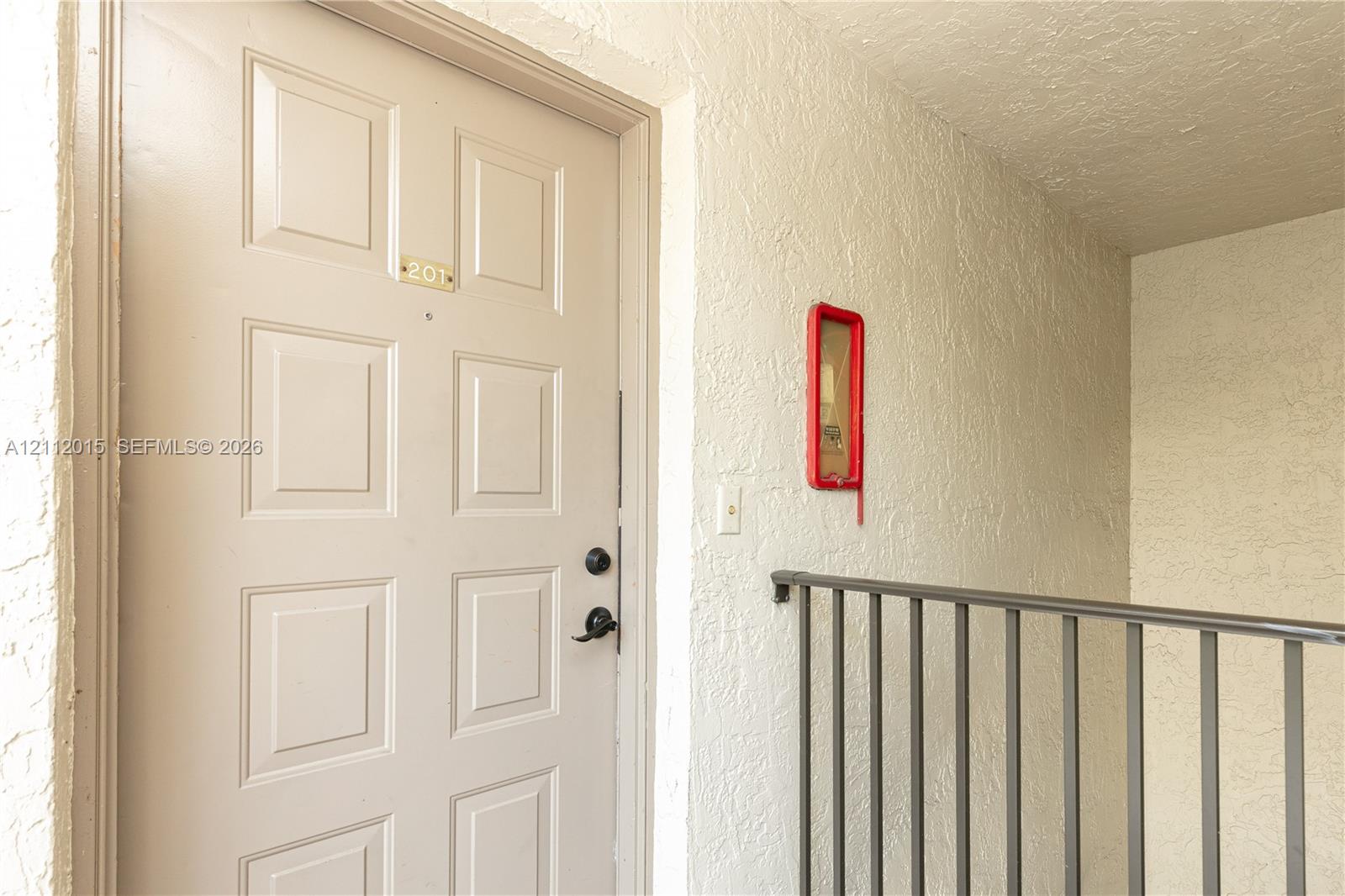 Entryway featuring a solid-core, six-panel door with integrated lock hardware and a textured stucco wall finish