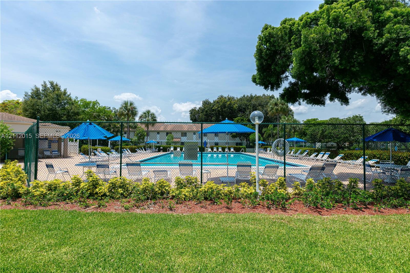 Swimming pool with a paved deck, perimeter fencing, mature landscaping, and green space