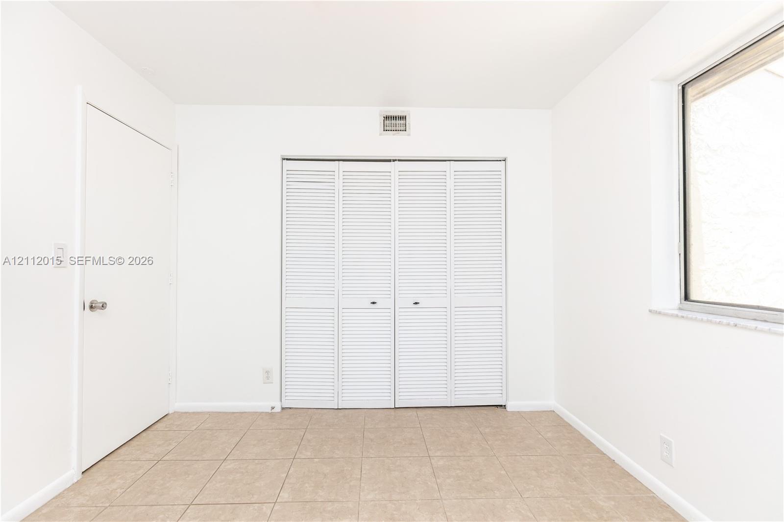Interior space featuring neutral tile flooring, a four-panel louvered closet, and a single-hung window with a stone-finish sill