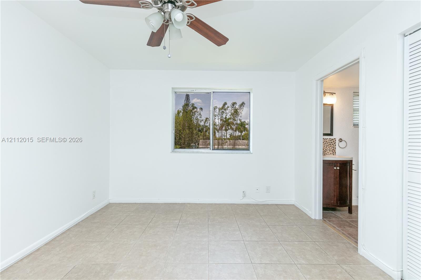 Room featuring neutral tile flooring, a central ceiling fan with integrated lighting, a sliding window, and a louvered closet door
