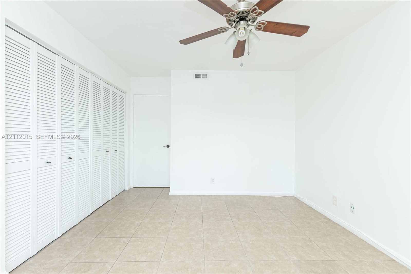 Neutral-toned ceramic tile flooring, multi-panel louvered closet doors, and a ceiling-mounted fan with integrated lighting
