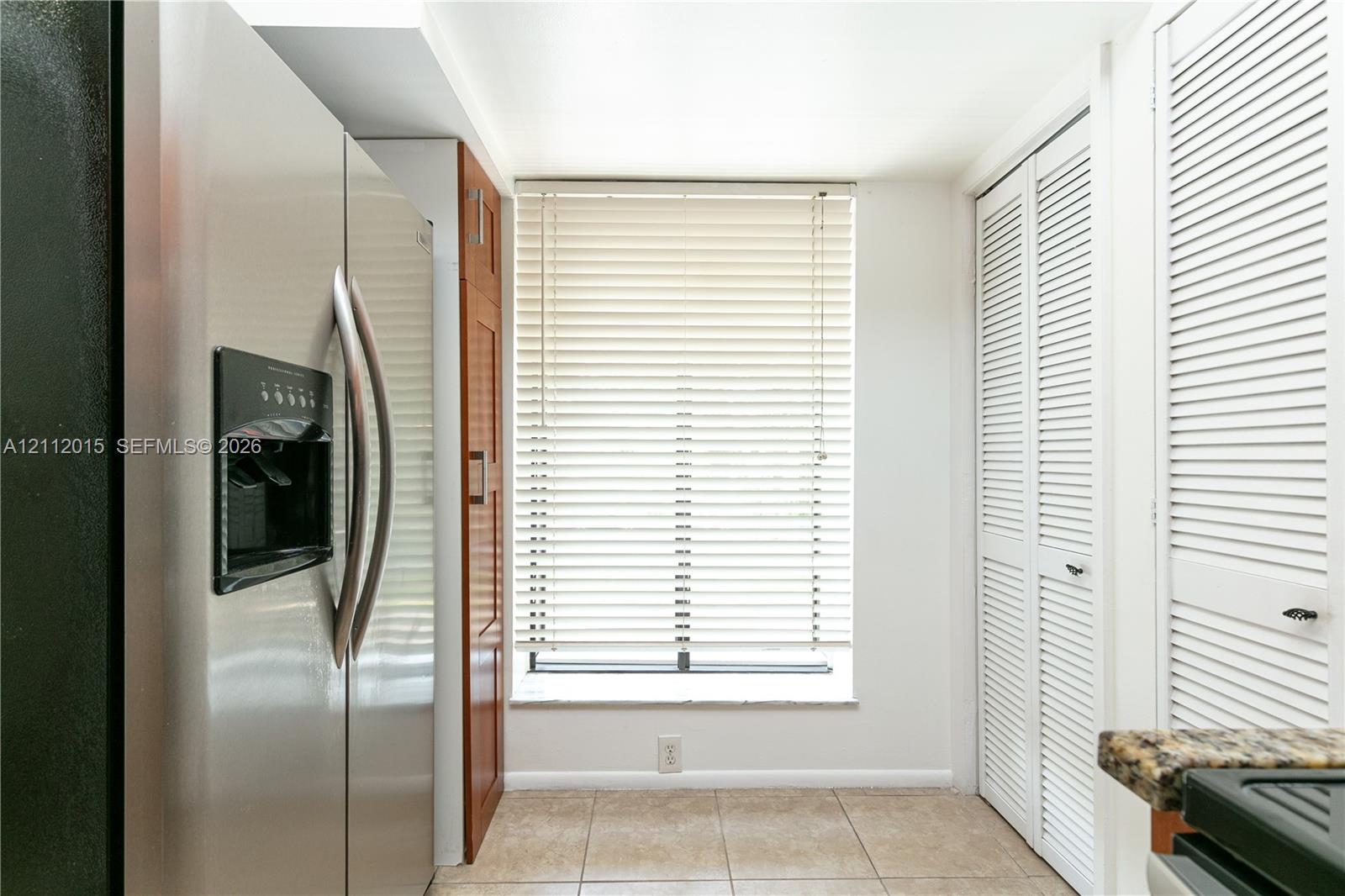 Stainless steel side-by-side refrigerator, built-in wooden cabinetry, tile flooring, and white louvered closet doors