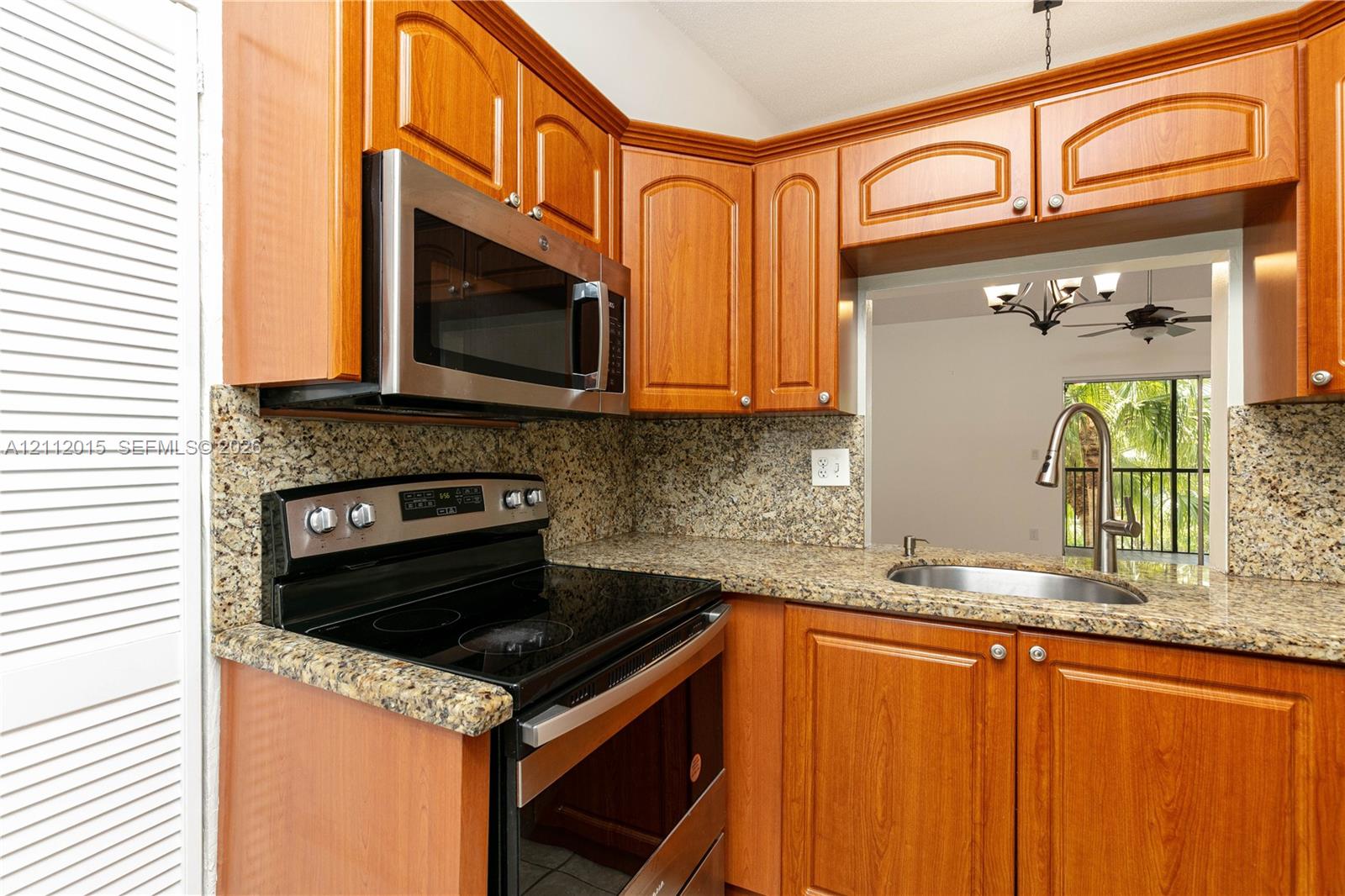 Kitchen featuring wood-finish cabinetry, stone-patterned countertops, stainless steel microwave, electric range, and an undermount sink with a high-arch faucet