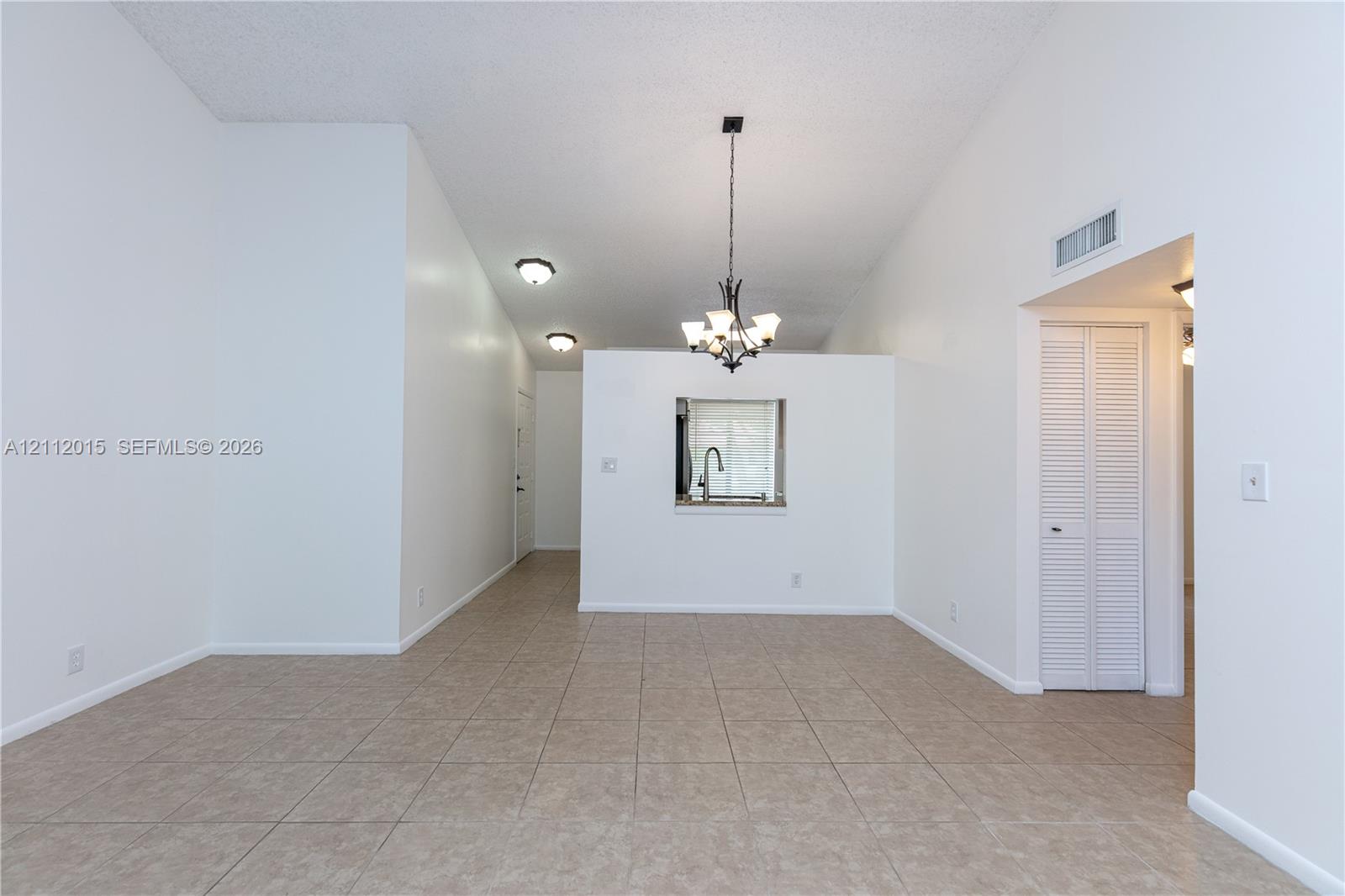 Vaulted ceilings, neutral tile flooring, iron-finish chandelier, recessed lighting, and built-in louvered closet doors