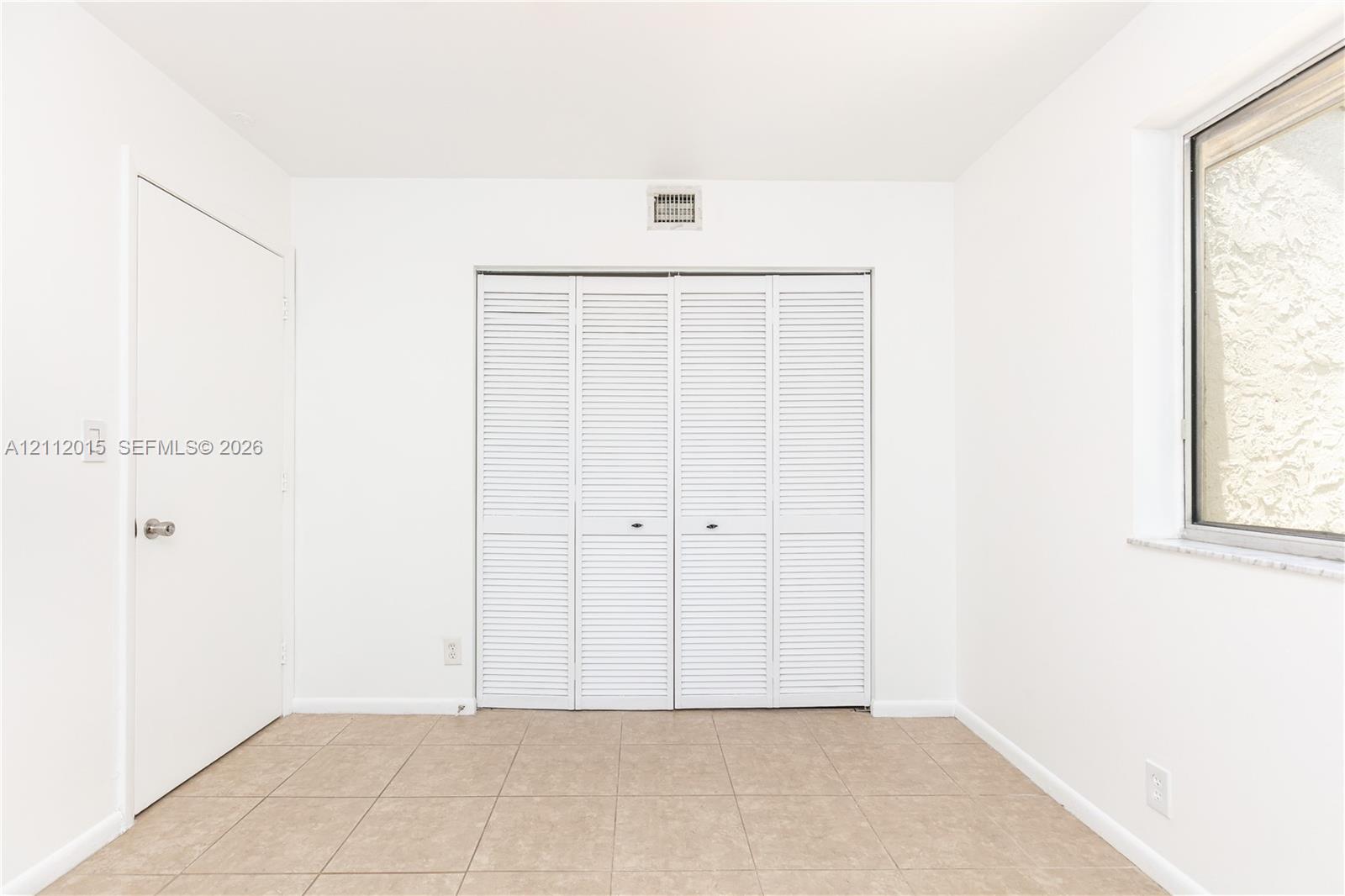 Neutral interior space featuring tile flooring, a multi-panel closet with louvered doors, a solid-panel door, and a window with a stone sill