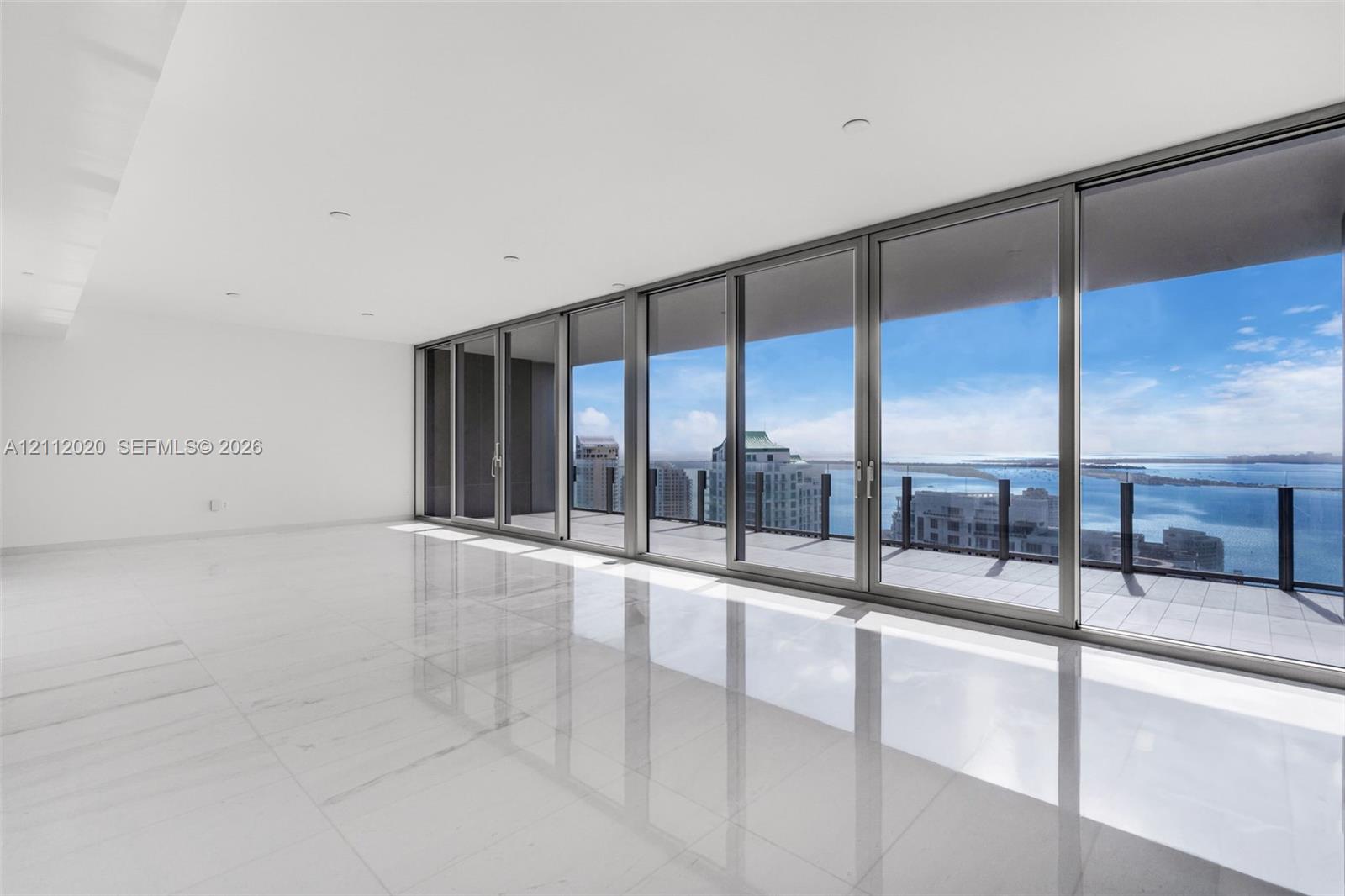 Floor-to-ceiling sliding glass doors, expansive private terrace with glass railing, large-format polished tile flooring, recessed ceiling lighting, and panoramic water and city scenery