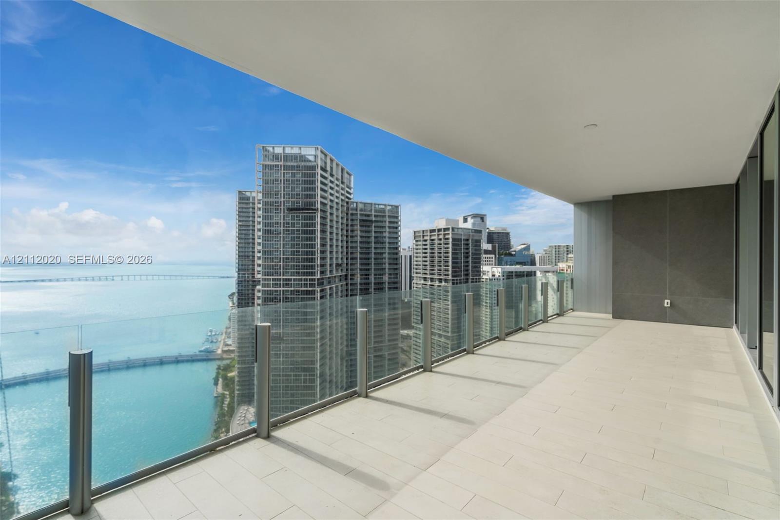Expansive covered balcony featuring large-format tile flooring, a frameless glass railing, and structural concrete ceiling