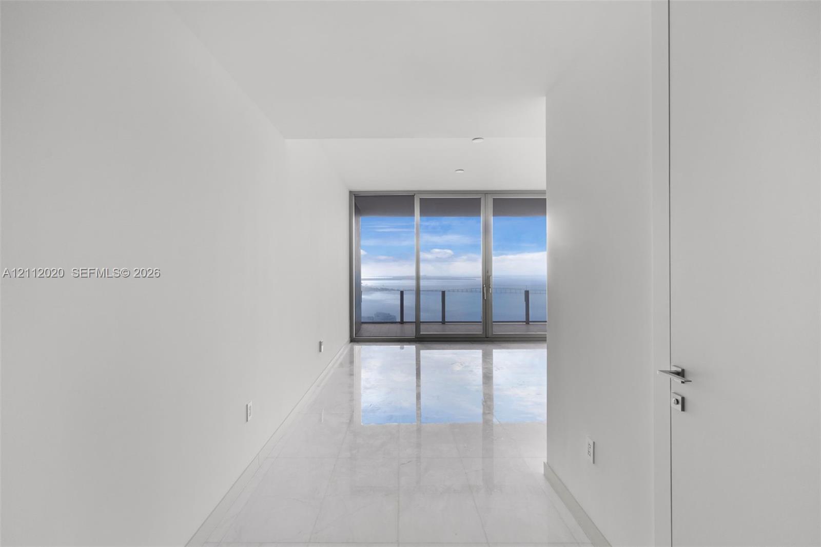 Minimalist interior featuring large-format stone flooring, floor-to-ceiling glass sliding doors, and a private balcony with water scenery Minimalist interior featuring large-format stone flooring, floor-to-ceiling glass sliding doors, and a private balcony with water scenery