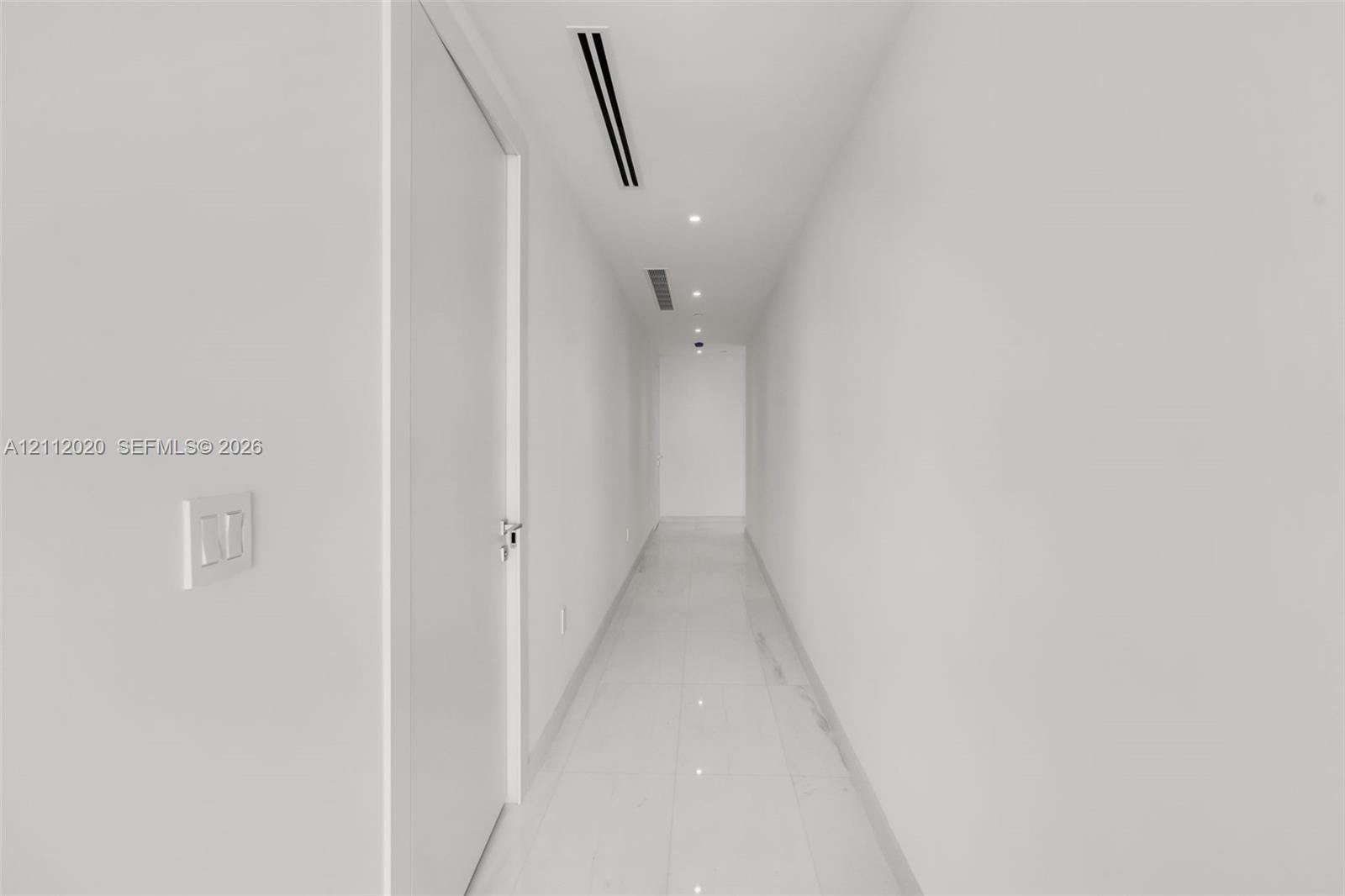 Minimalist hallway featuring white tile flooring, flush-mount recessed lighting, and integrated linear ceiling components