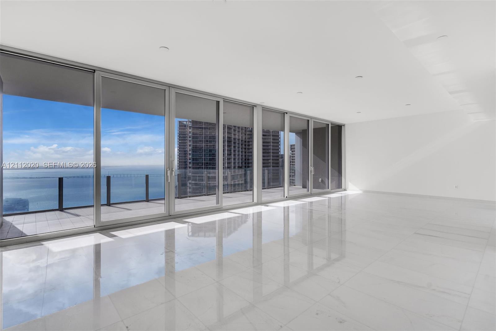 Floor-to-ceiling glass sliding doors, polished tile flooring, recessed lighting, and expansive balcony space with water and urban skyline scenery Floor-to-ceiling glass sliding doors, polished tile flooring, recessed lighting, and expansive balcony space with water and urban skyline scenery